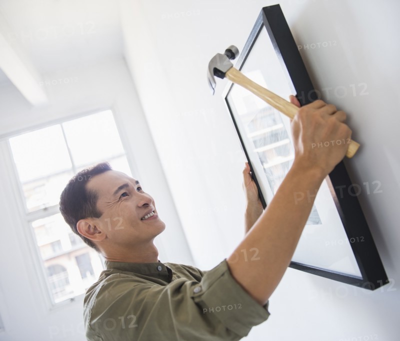 Mid adult man hanging picture on wall. Photo: Daniel Grill