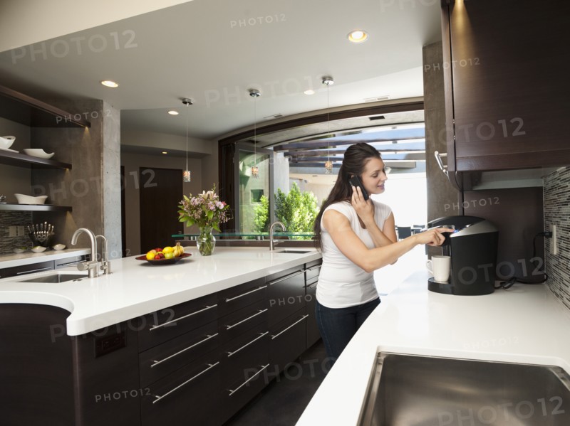 Young woman making morning coffee while using mobile phone. Photo: Erik Isakson