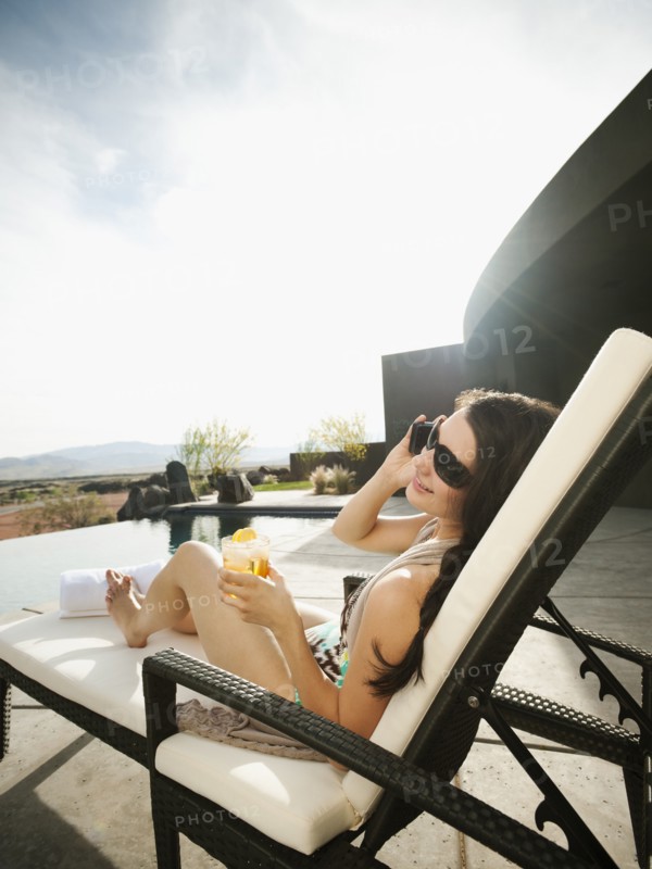 Young attractive woman using mobile phone while sitting by swimming pool.