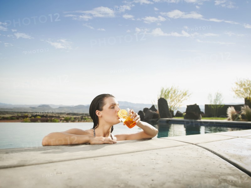 Young attractive woman enjoying cocktail on edge of swimming pool.