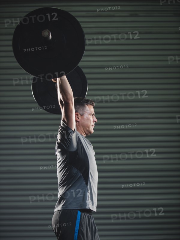 Mature man lifting heavy barbell .