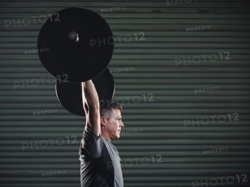 Mature man lifting heavy barbell .