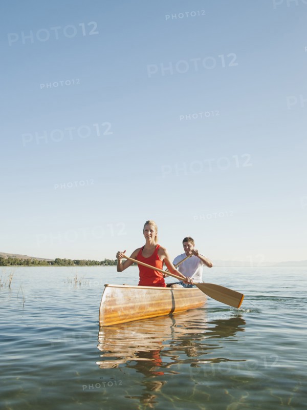 Portrait of two young people paddling canoe.