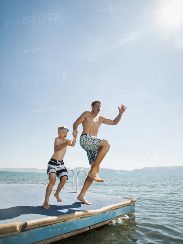 Father and son (4-5) jumping into lake caught.