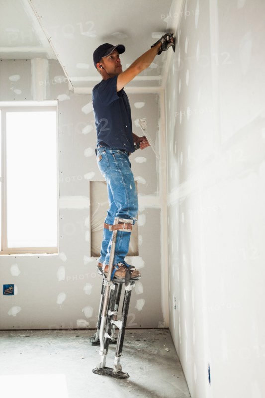 Drywall worker on stilts working on drywall joints. Photo : Mike Kemp