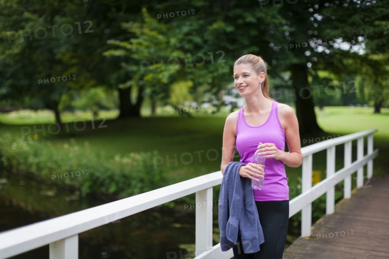 Young woman walking on a bridge after running and holding a towel and a bottle of water