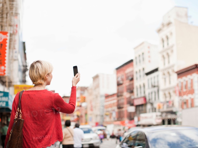 Woman taking picture with her mobile phone on street. Photo : Jessica Peterson