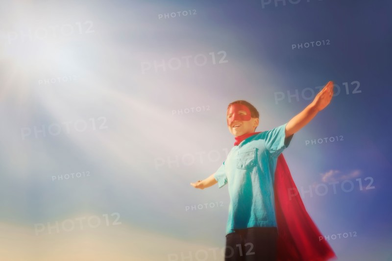 Boy (6-7) in superhero costume under blue sky.