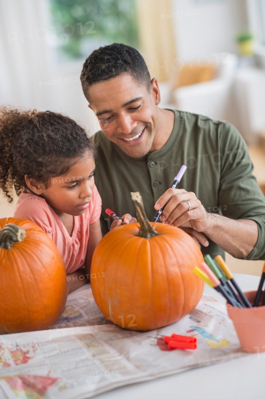 Father and daughter (6-7) carving pumpkins for Halloween.