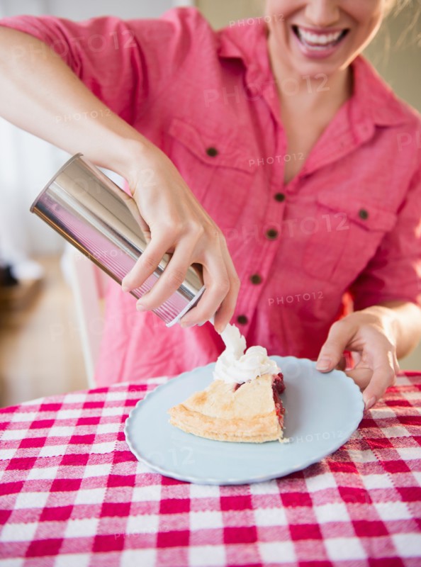 Young woman applying whipped cream on cherry pie