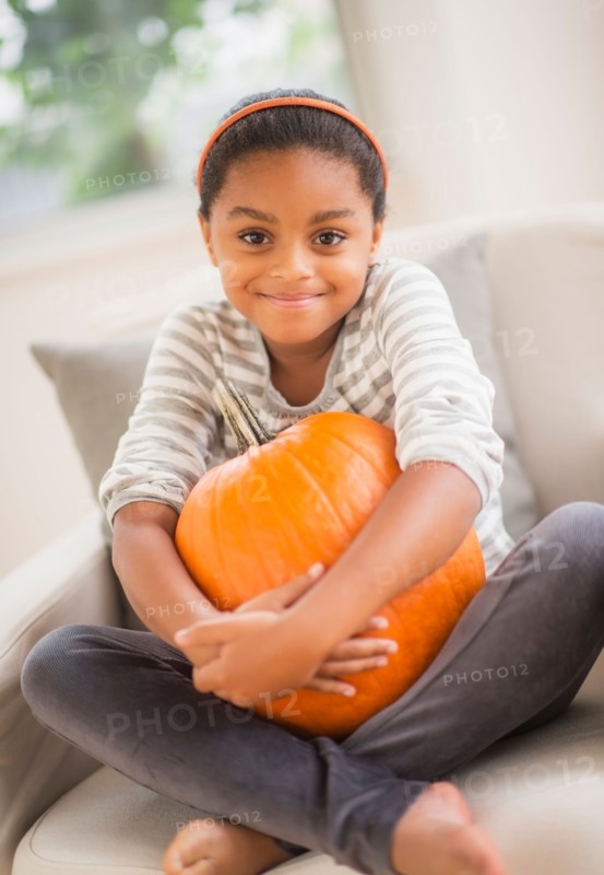 Portrait of smiling girl (6-7) sitting on sofa with pumpkin