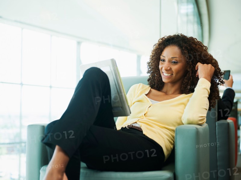 Smiling woman using digital tablet while waiting in lobby