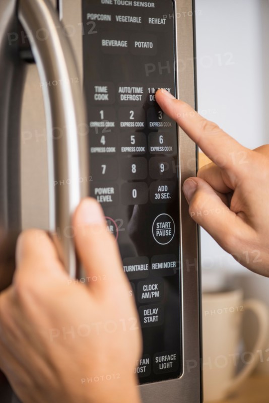 Close-up of hand using microwave oven.