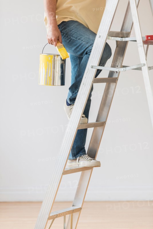 Man holding paint can and climbing ladder.