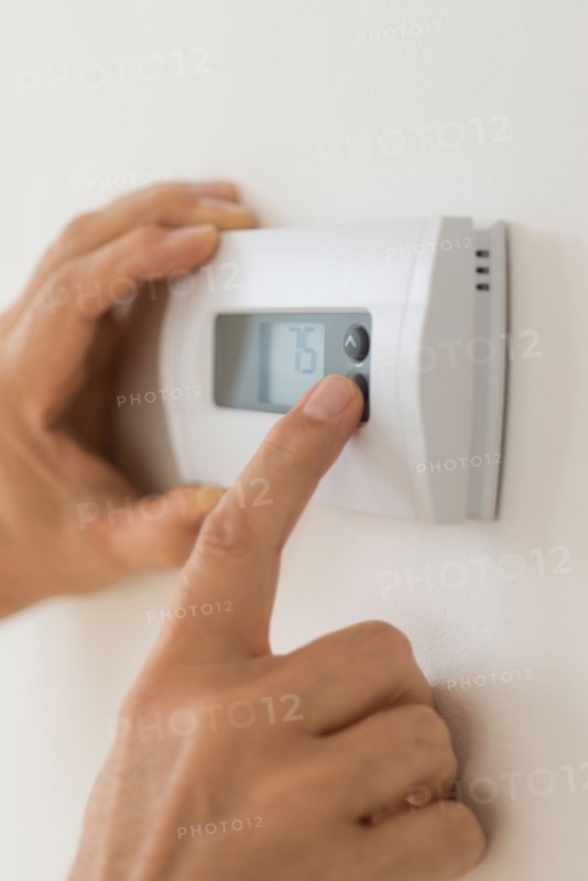 Hand changing settings on air conditioning thermostat.