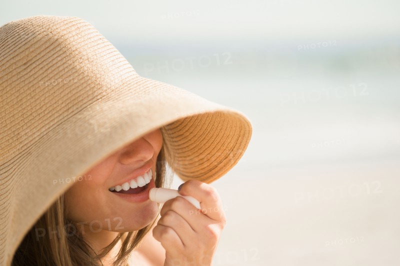 Woman wearing sun hat applying lipstick. Photo: Jamie Grill