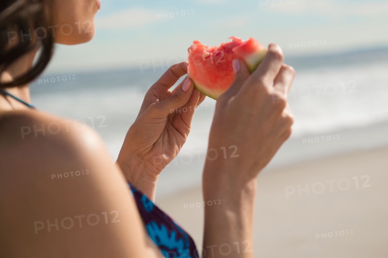 Woman eating watermelon at beach. Photo : Jamie Grill