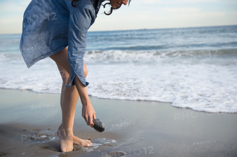 Woman collecting seashells on beach. Photo : Jamie Grill