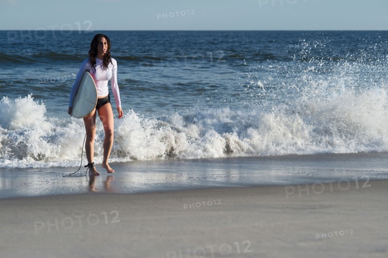 Woman carrying surfboard on beach. Photo : Jamie Grill