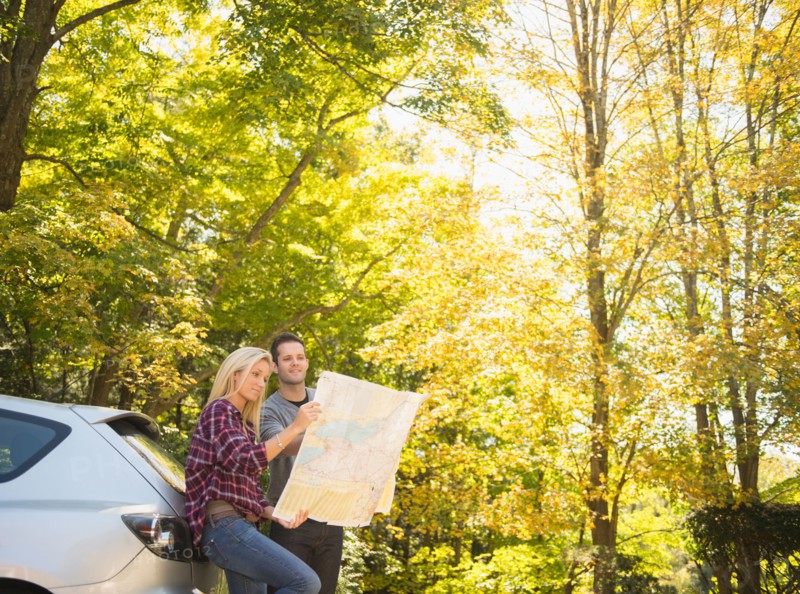 Couple leaning against car and reading map. Photo : Jamie Grill