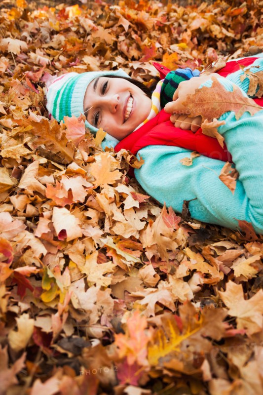 Portrait of smiling young woman lying on autumn leaves . Photo : Mike Kemp
