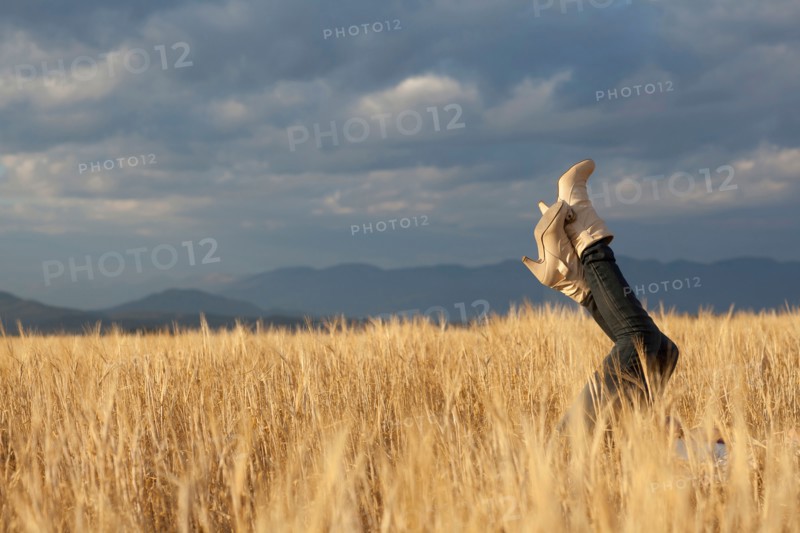 Woman lying in scenic field with feet in air. Photo : Noah Clayton
