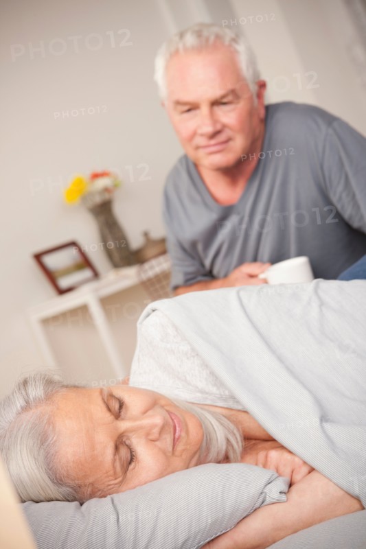 Senior man with coffee cup looking at sleeping wife. Photo: Rob Lewine
