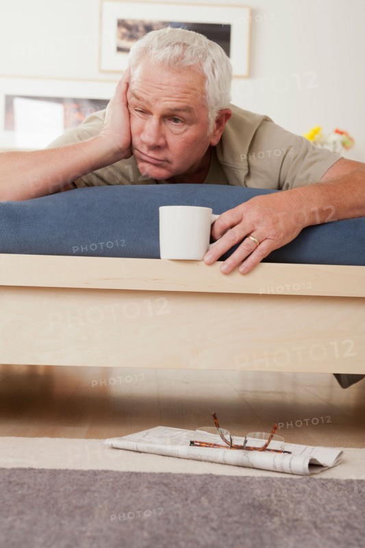 Tired senior man holding coffee cup lying on bed . Photo: Rob Lewine