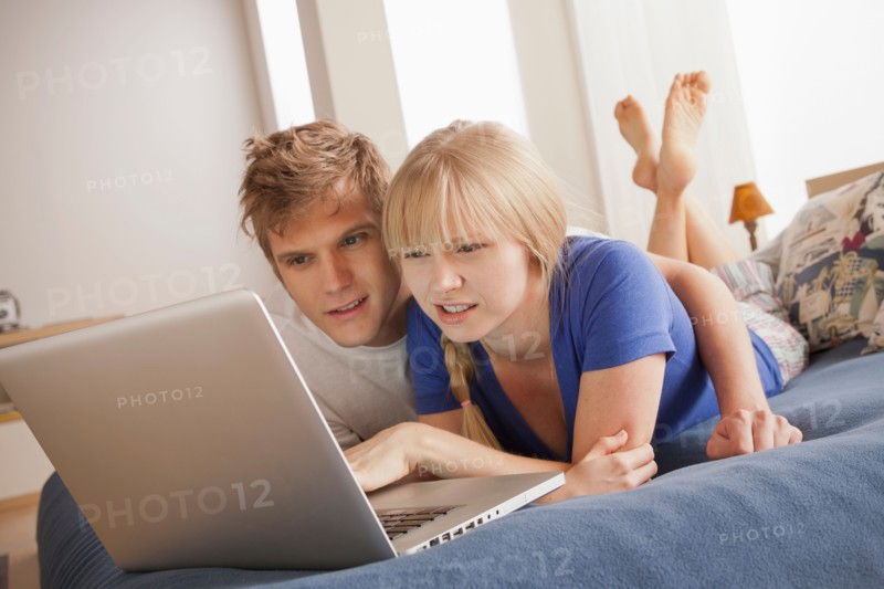 Couple lying on bed using laptop. Photo: Rob Lewine