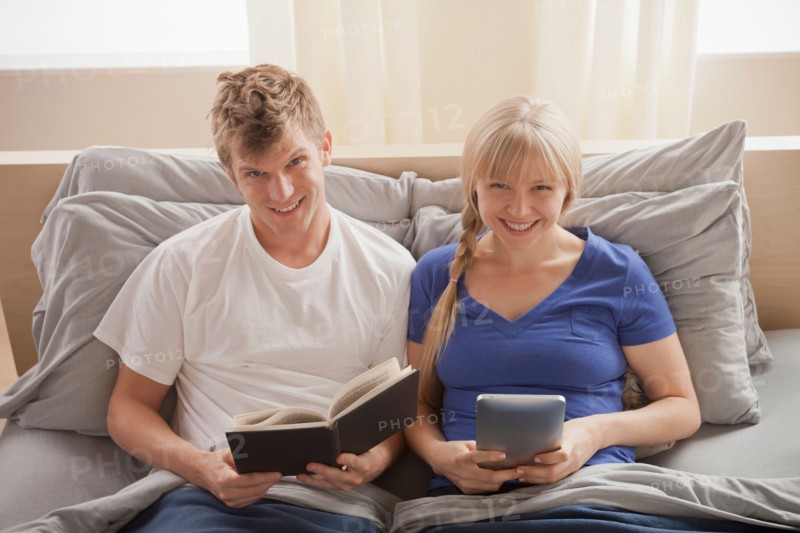 Portrait of couple sitting in bed reading. Photo : Rob Lewine