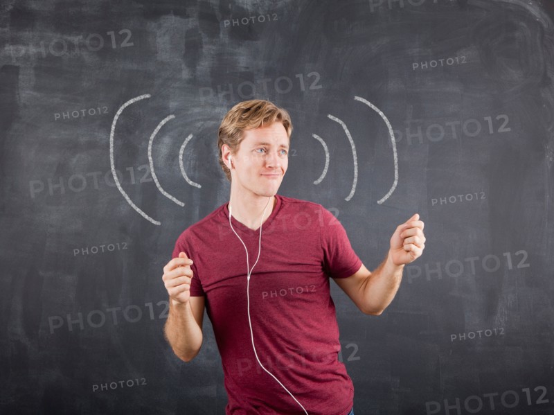 Studio shot of mid adult man listening to music on earphones and dancing with chalk drawing on blackboard. Photo : Jessica Peterson