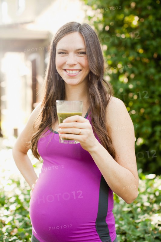 Portrait of pregnant mid adult woman in sport clothing holding glass with green juice. Photo: Jessica Peterson