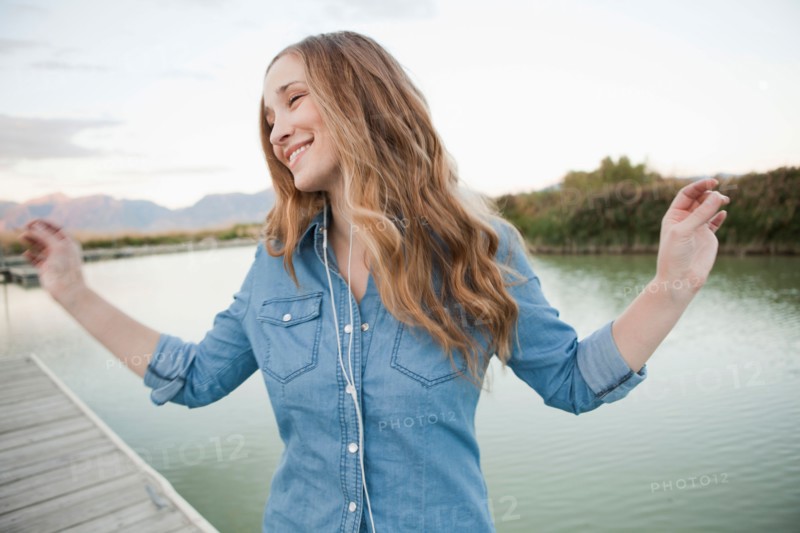 Portrait of young woman listening to mp3 player on jetty. Photo : Jessica Peterson