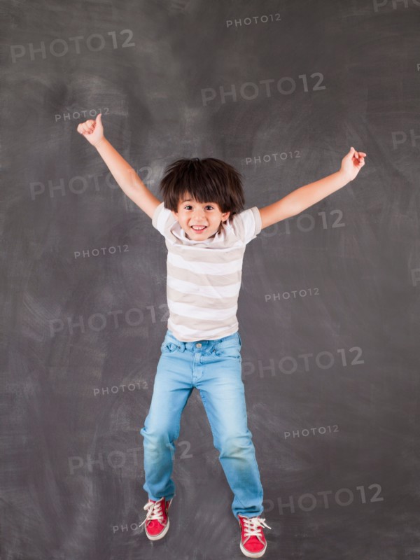 Studio portrait of boy (6-7) jumping in front of blackboard. Photo : Jessica Peterson