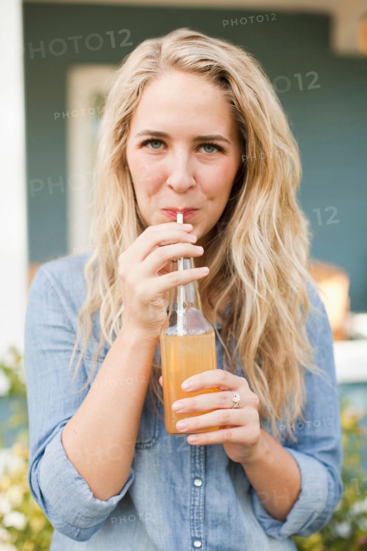 Front view portrait of young woman drinking soda through drinking straw. Photo : Jessica Peterson
