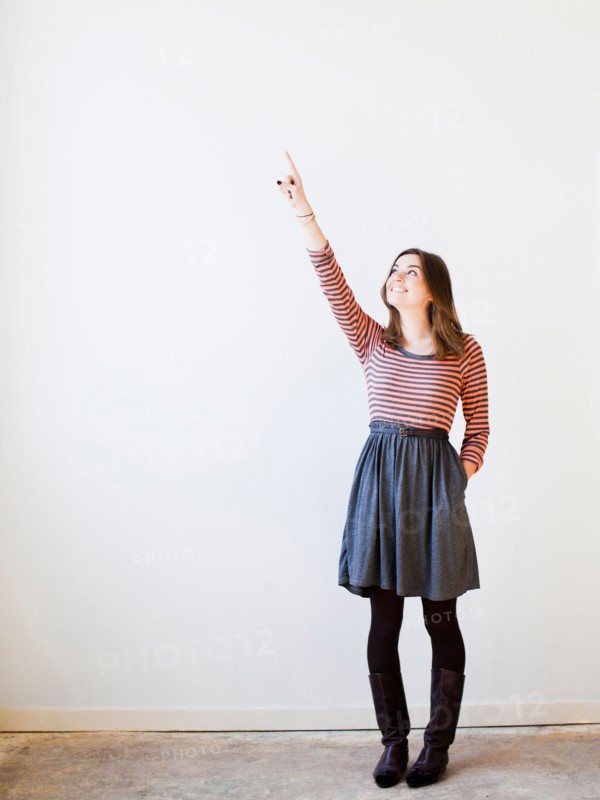 Studio shot young woman looking up and pointing. Photo : Jessica Peterson