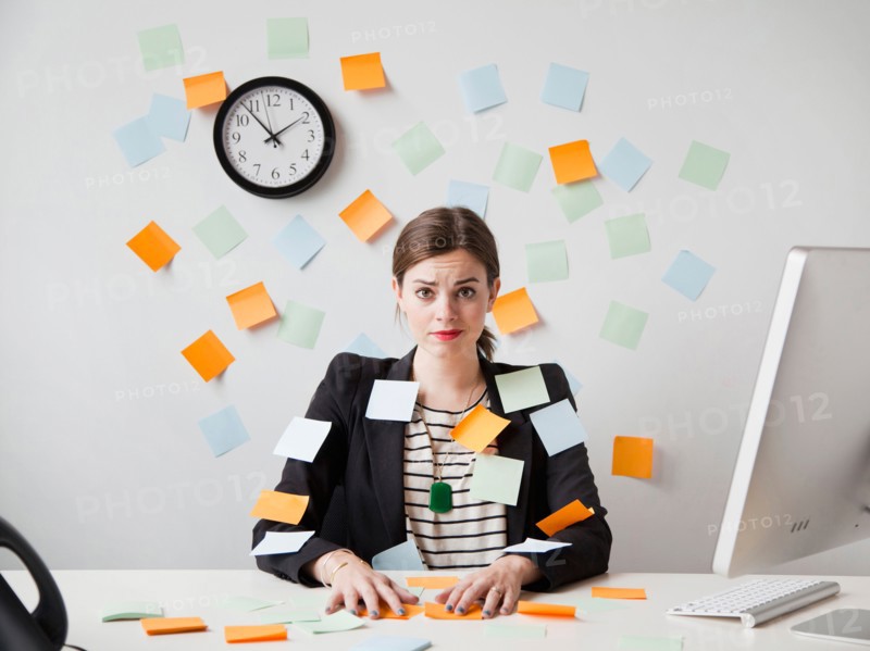 Studio shot of young woman working in office covered with adhesive notes. Photo: Jessica Peterson