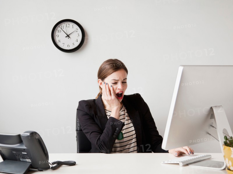 Studio shot of young woman working in office yawning. Photo : Jessica Peterson