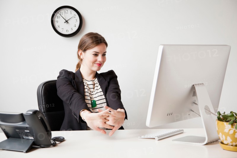 Studio shot of young woman working in office and stretching her arms. Photo: Jessica Peterson