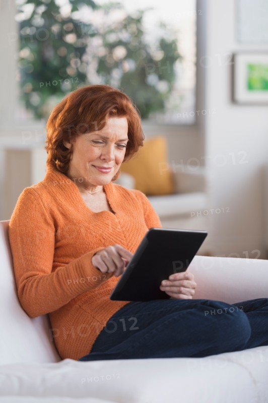 Woman sitting on sofa using digital tablet.