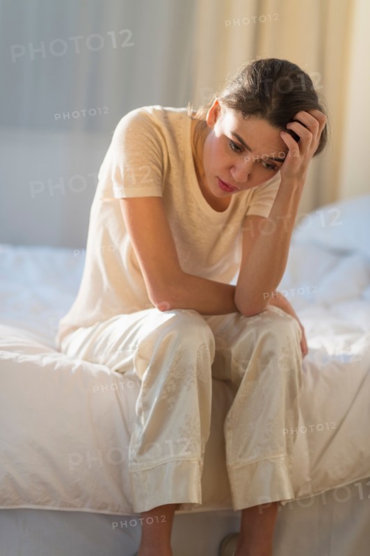Young woman sitting on bed with headache.