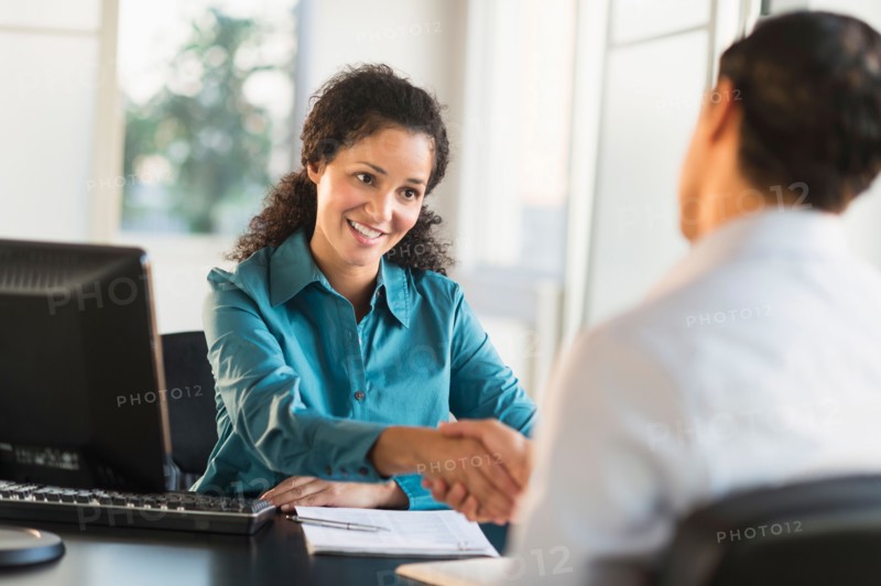 Woman shaking hand with man at desk.
