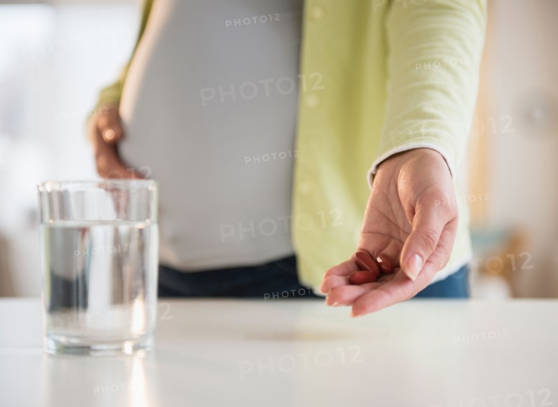 Pregnant woman holding medicine with glass of water in front
