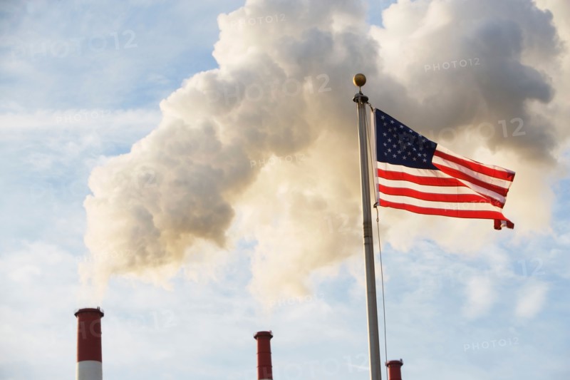 American flag in front of smoke stacks