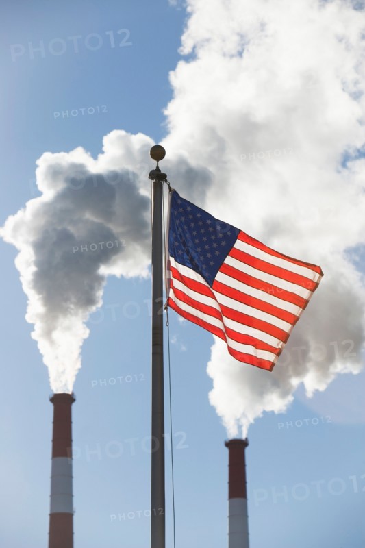American flag in front of smoke stacks