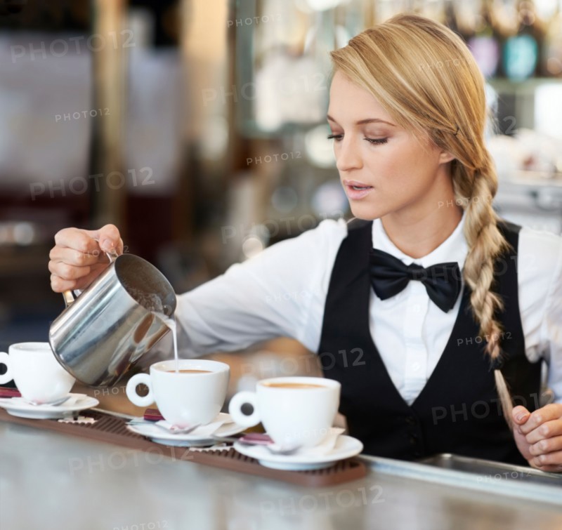 Female barista pouring milk into coffee cup