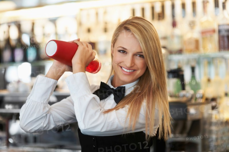 Young female bartender using cocktail shaker