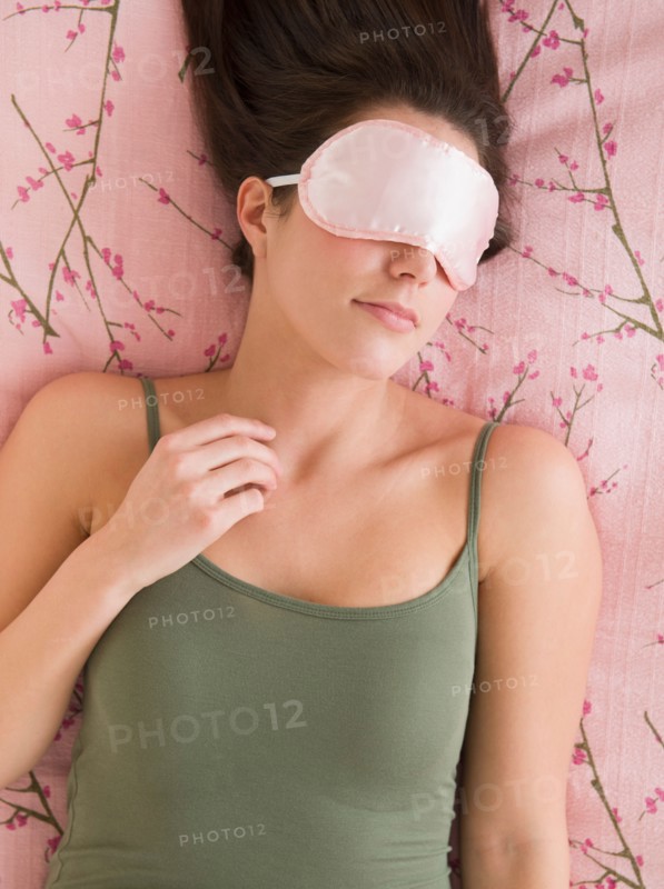 Woman with sleep mask lying on bed .
