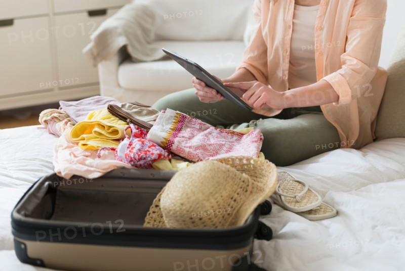 Woman using digital tablet while packing suitcase.