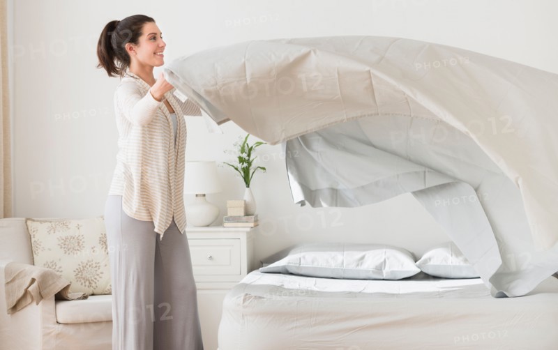 Woman spreading sheet on bed.